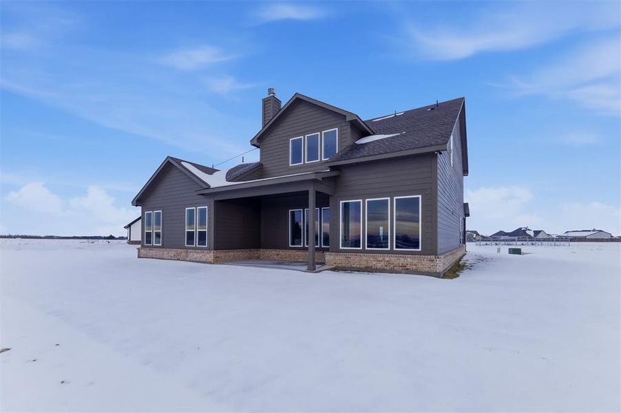 Snow covered back of property with a patio area, a chimney, and a shingled roof