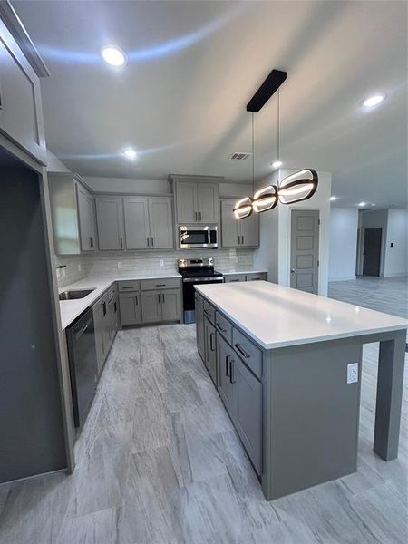 Kitchen featuring gray cabinetry, electric stove, decorative backsplash, a kitchen island, and light countertops Kitchen featuring gray cabinetry, electric stove, decorative backsplash, a kitchen island, and light countertops