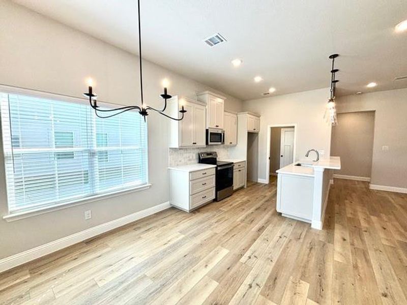 Kitchen with pendant lighting, white cabinets, a center island with sink, sink, and stainless steel appliances