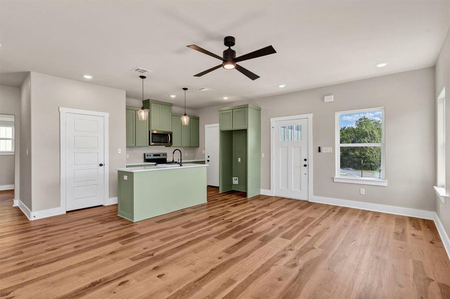 Kitchen featuring green cabinets, light countertops, a center island with sink, light wood-style flooring, and recessed lighting