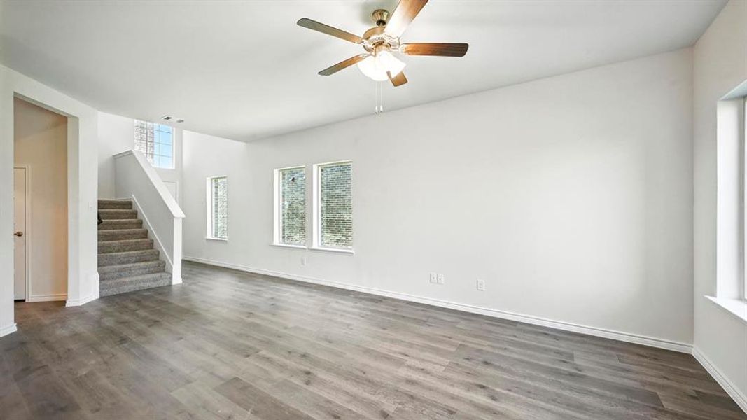 Unfurnished living room featuring stairway, dark wood-style flooring, and a ceiling fan