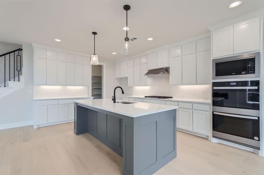 Kitchen featuring a center island with sink, sink, white cabinets, and decorative backsplash