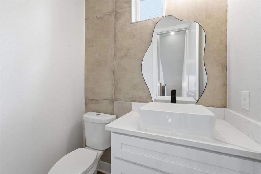 Modern powder bath featuring a sleek vessel sink vanity, designer mirror, and elegant tile accent wall for a refined contemporary look.