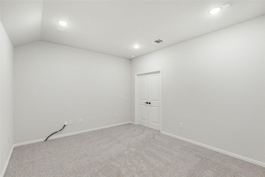 Empty room with gray carpet, white walls, recessed lighting, and a paneled door