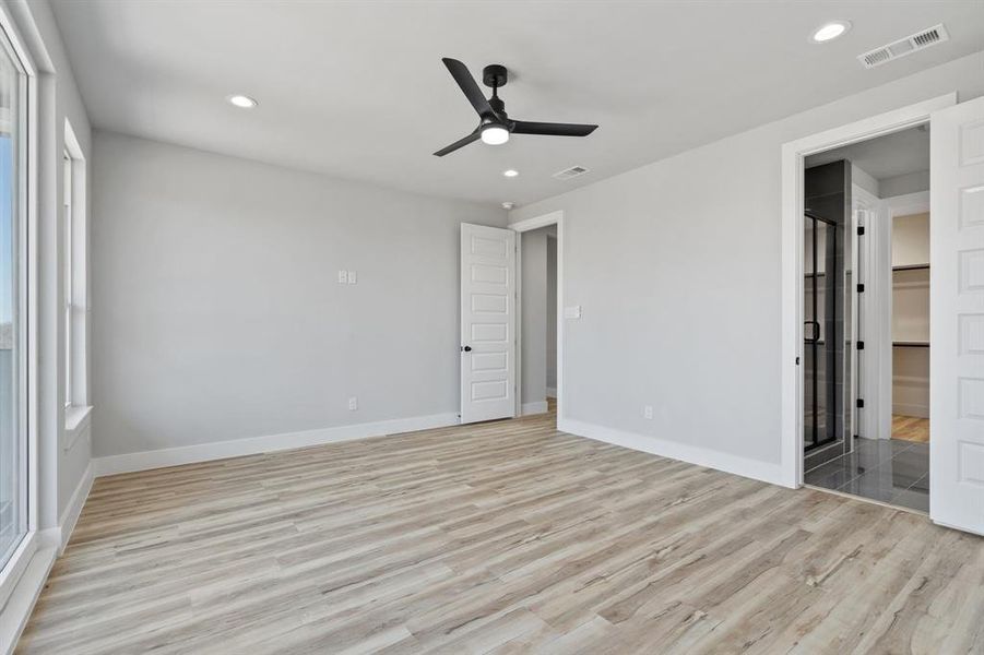 Unfurnished bedroom featuring multiple windows, light wood-type flooring, connected bathroom, and ceiling fan