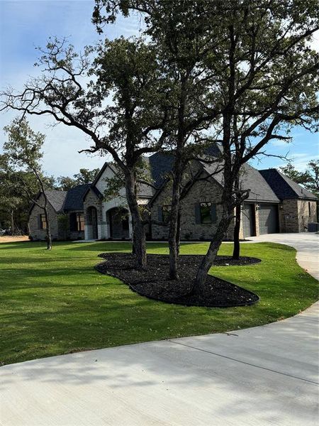 French provincial home featuring stone siding, a front lawn, and driveway French provincial home featuring stone siding, a front lawn, and driveway