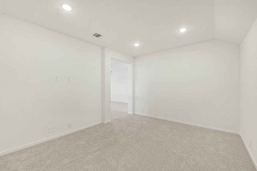 Empty bedroom with white walls, beige carpet, recessed lighting, and open doorway to hallway