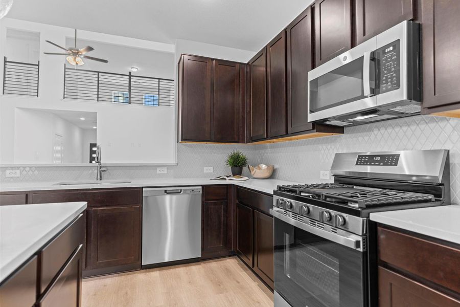 Close-up of the chef-style kitchen showcasing Quartz countertops, built-in microwave, gas range, and 42" upper cabinets that offer both storage and sleek style. **Image Representative of Plan Only and May Vary as Built**.