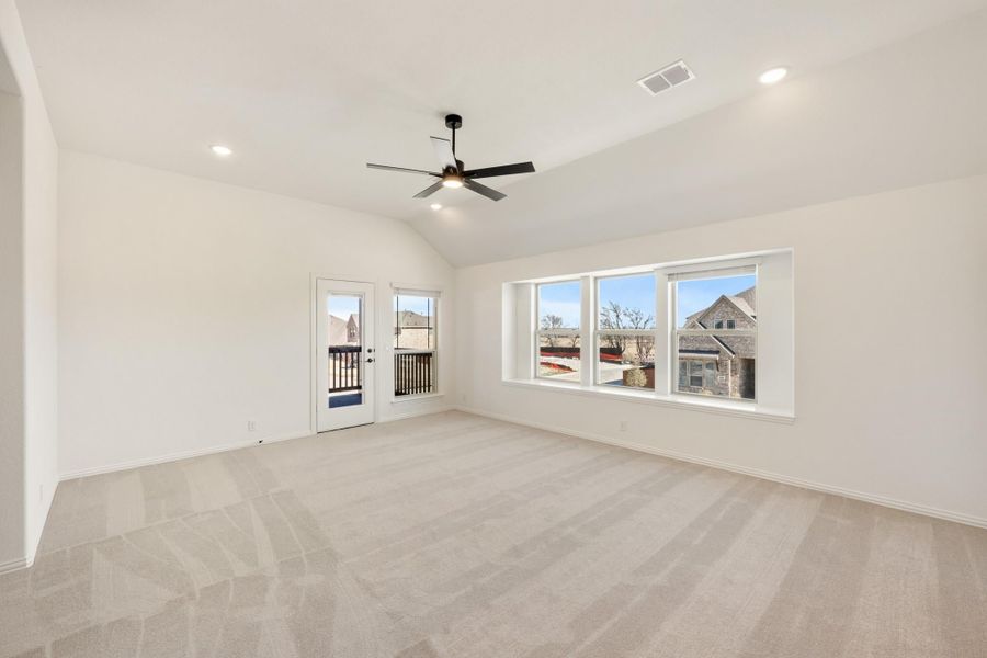 Empty living room with vaulted ceiling, ceiling fan, carpet flooring, and large windows with backyard door access.