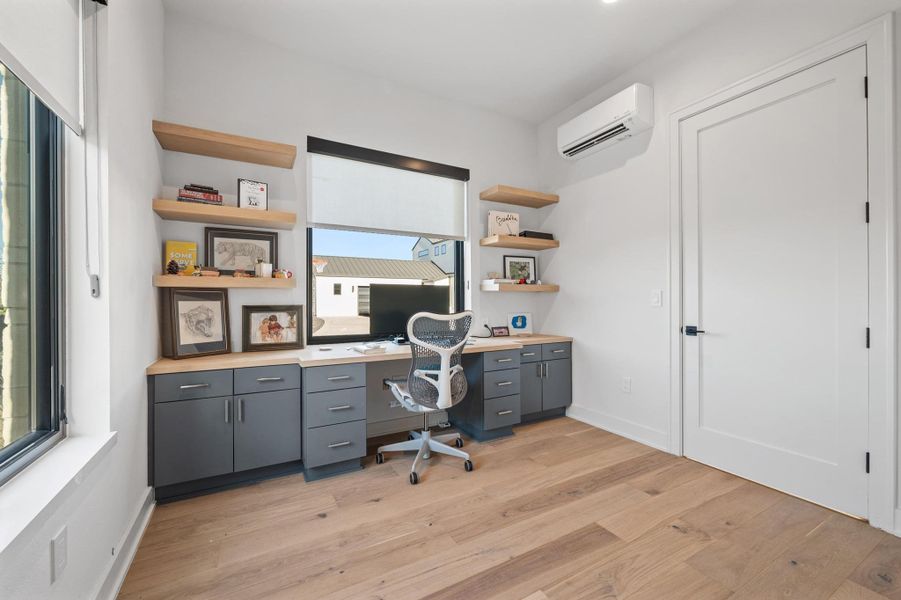 Office area featuring built in study area, baseboards, a wall mounted air conditioner, and light wood finished floors Office area featuring built in study area, baseboards, a wall mounted air conditioner, and light wood finished floors