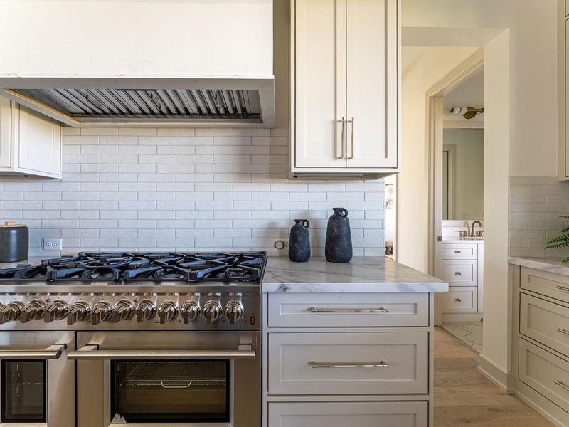 Kitchen featuring exhaust hood, range with two ovens, backsplash, light stone counters, and light wood-style flooring
