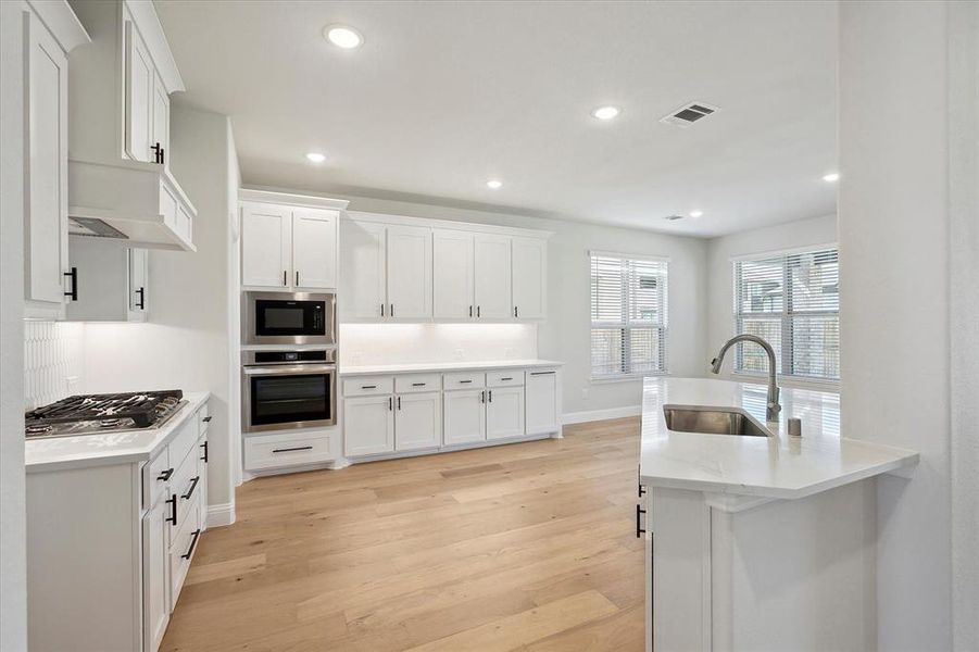 Kitchen with stainless steel appliances, a sink, light wood-style flooring, white cabinets, and recessed lighting