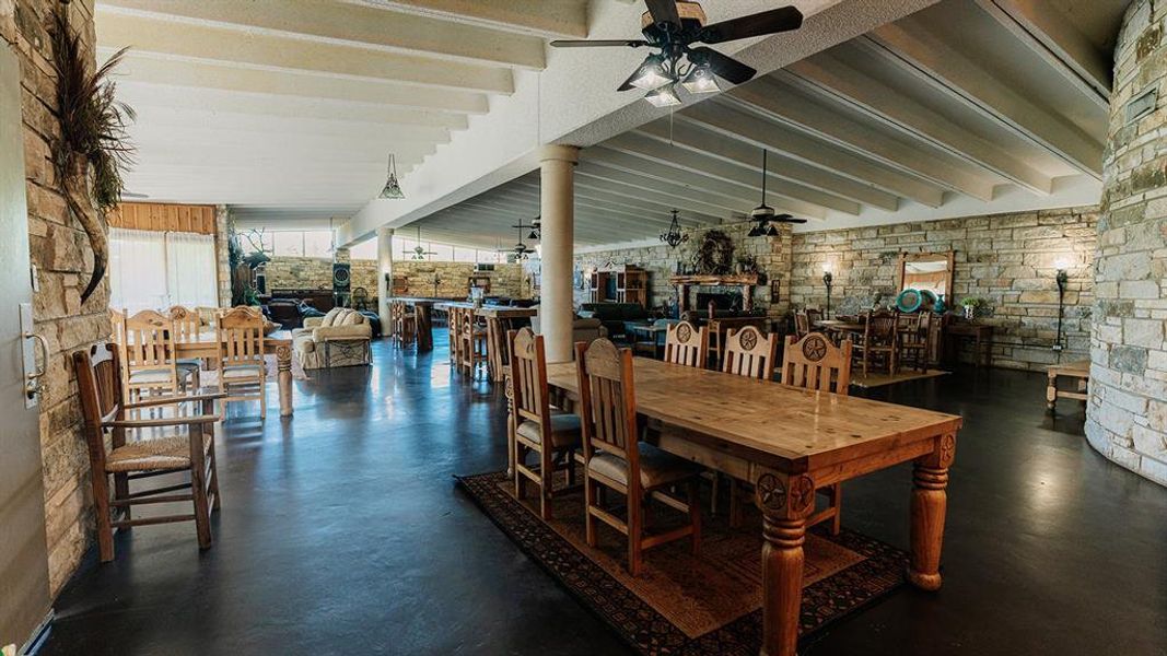 Dining area featuring beamed ceiling, a ceiling fan, a fireplace, and concrete floors