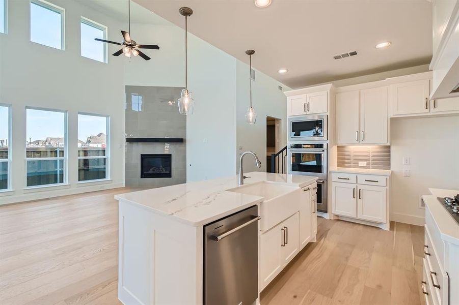 Kitchen with light stone countertops, appliances with stainless steel finishes, white cabinetry, a high ceiling, and a center island with sink