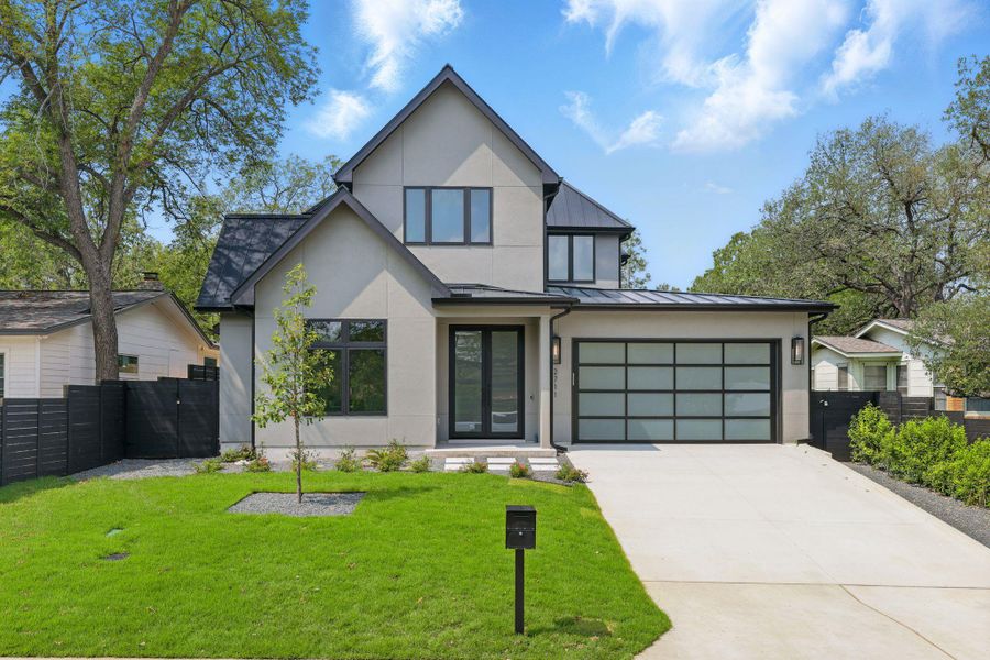 View of front of home with stucco siding, a standing seam roof, driveway, a metal roof, and an attached garage