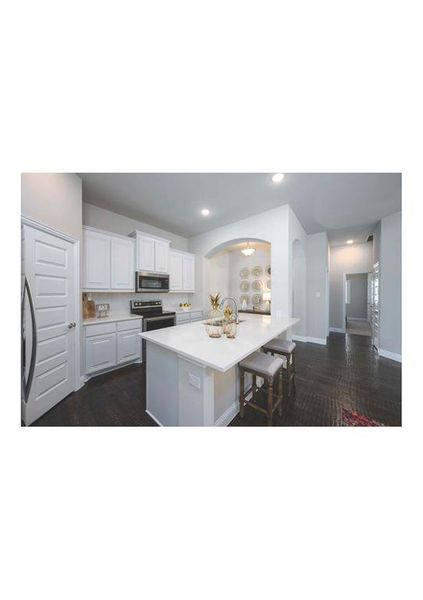 Kitchen with dark hardwood / wood-style flooring, stainless steel appliances, a center island with sink, white cabinets, and a breakfast bar area