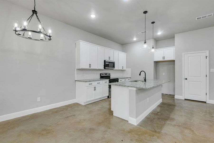 Kitchen featuring stainless steel appliances, concrete floors, a center island with sink, white cabinetry, and light stone countertops