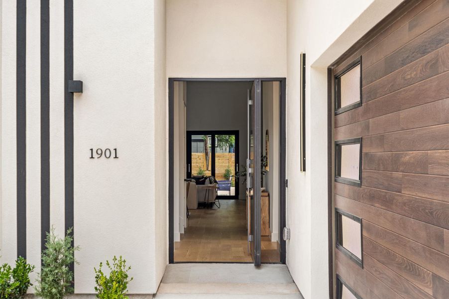 A modern facade with bold black accents welcomes you, featuring a rich wood-paneled door with rectangular glass inserts. A modern facade with bold black accents welcomes you, featuring a rich wood-paneled door with rectangular glass inserts.
