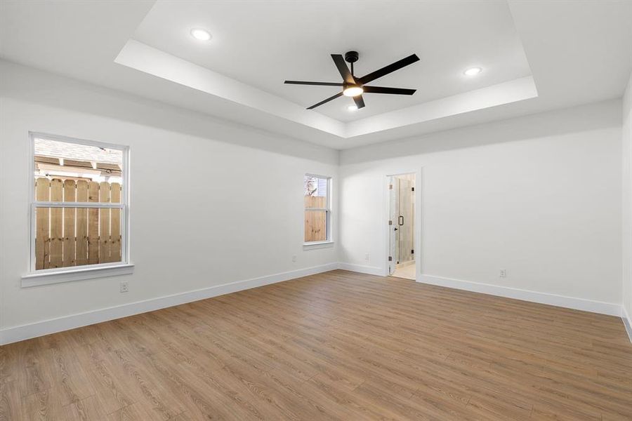 Empty room with baseboards, a tray ceiling, and wood finished floors