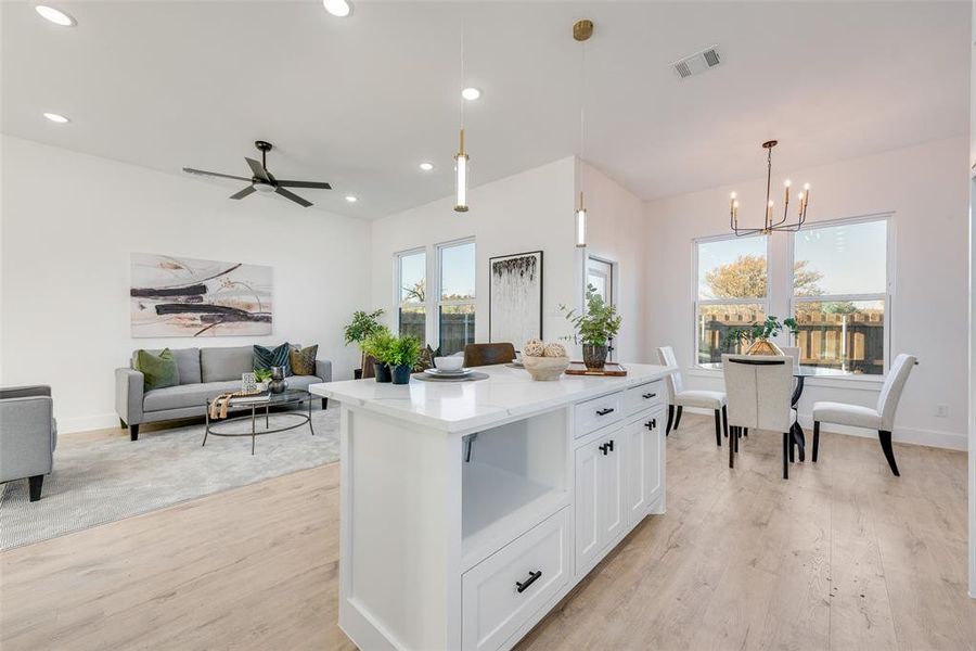 Kitchen with light wood-type flooring, ceiling fan with notable chandelier, pendant lighting, white cabinets, and a kitchen island