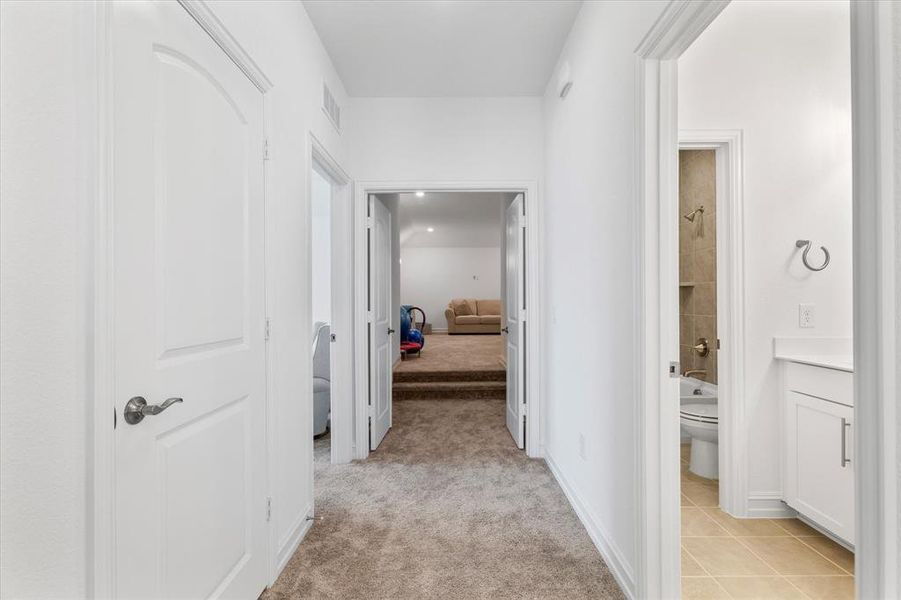 Carpeted hallway with white interior doors, leading to a sunken room with additional carpeting
