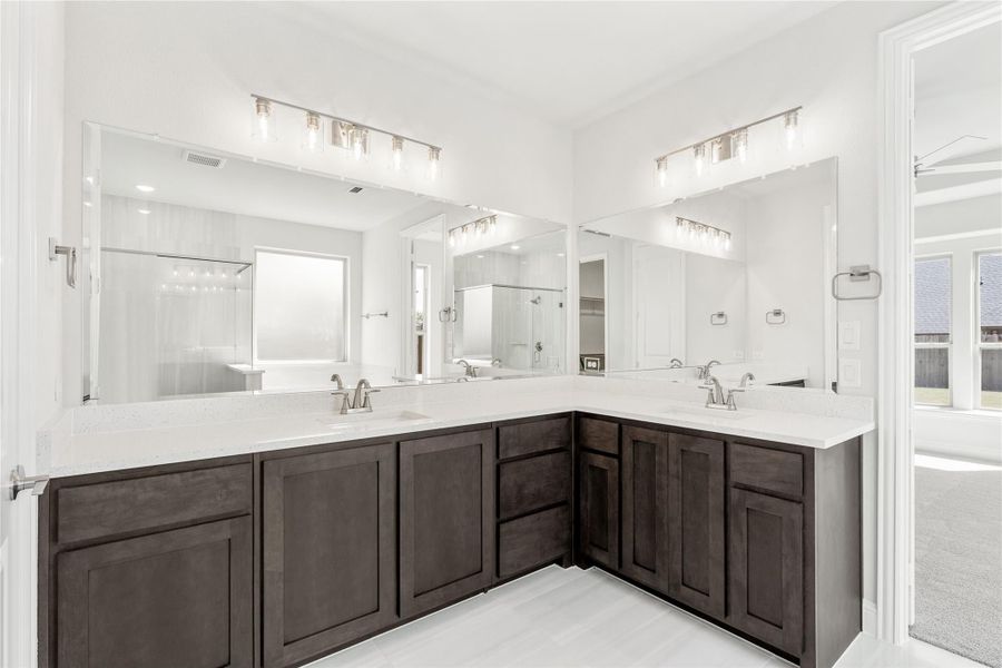 Master bathroom with L-shaped double vanity, dark wood cabinets, white countertops, and large mirrors with overhead lighting. Master bathroom with L-shaped double vanity, dark wood cabinets, white countertops, and large mirrors with overhead lighting.