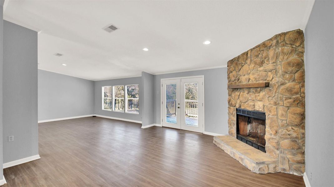 Unfurnished living room with french doors, a stone fireplace, crown molding, light wood finished floors, and recessed lighting