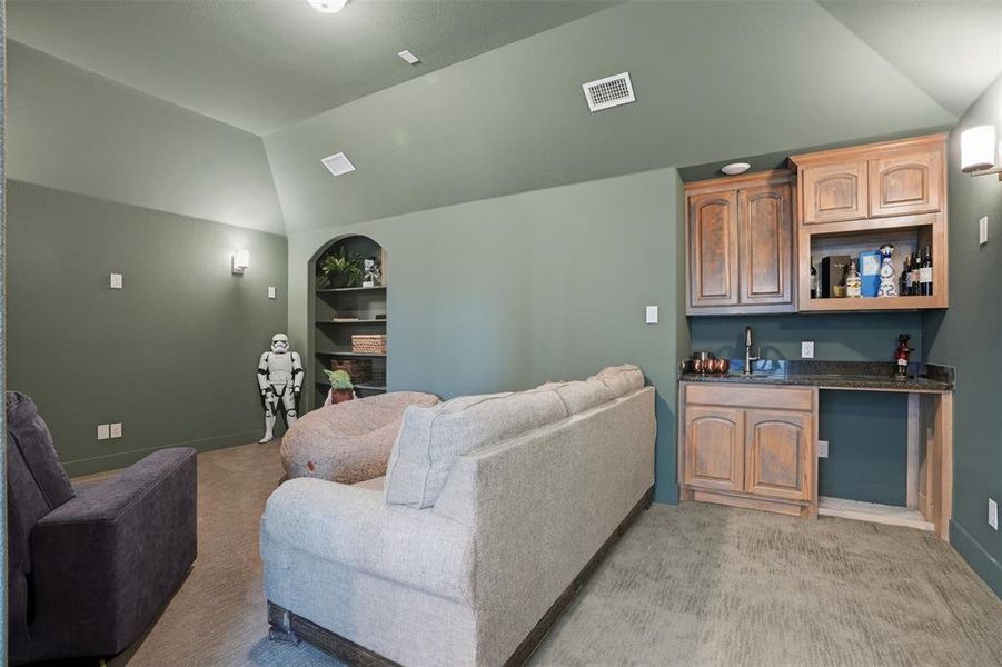 Home theater with lofted ceiling, light carpet, built in shelves, and bar with sink Home theater with lofted ceiling, light carpet, built in shelves, and bar with sink