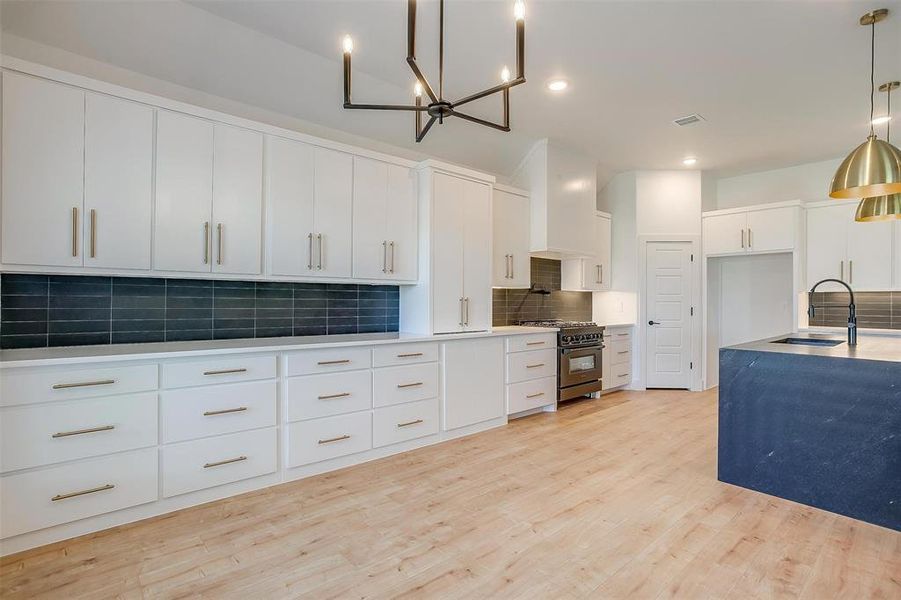 Kitchen with decorative light fixtures, light hardwood / wood-style flooring, range with gas stovetop, tasteful backsplash, and sink