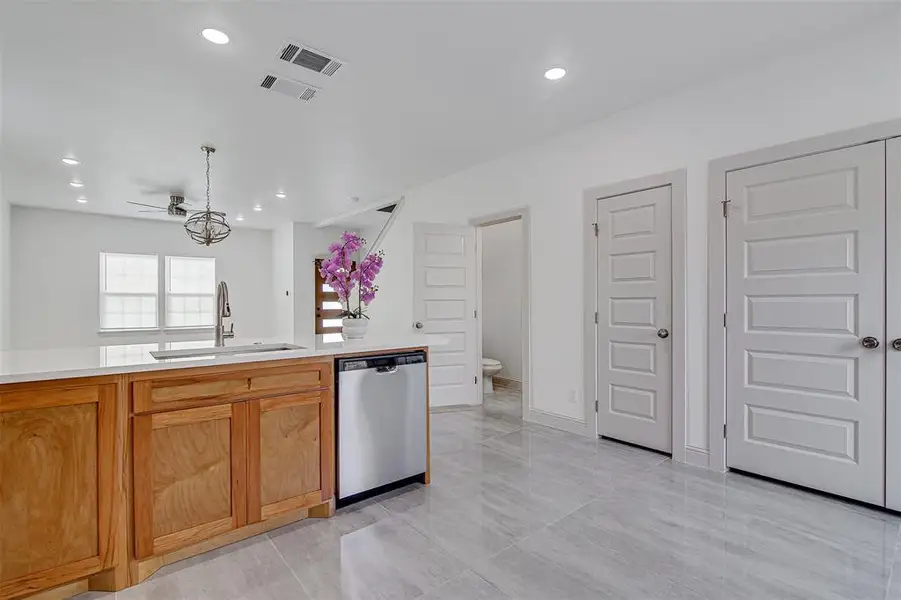 Kitchen with stainless steel dishwasher, brown cabinetry, hanging light fixtures, light stone counters, recessed lighting and marble flooring