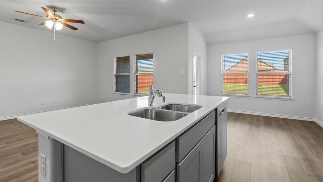 Kitchen with gray cabinets, light wood-type flooring, an island with sink, healthy amount of natural light, and recessed lighting