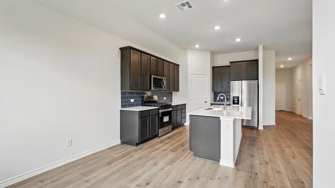 Open-concept kitchen featuring dark wood-finish cabinetry, stainless steel appliances, a center island with sink, and wood-finish flooring