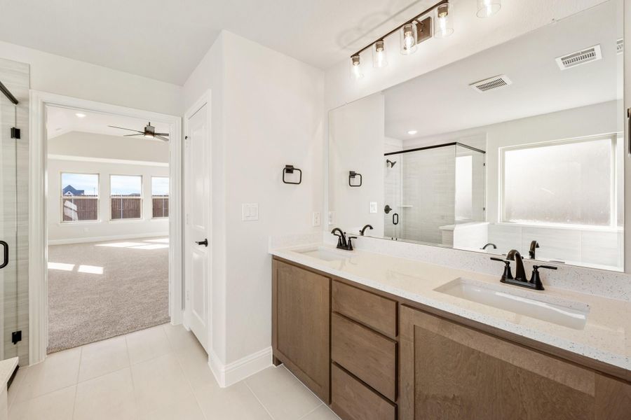 Master bathroom with double sink vanity, wood cabinets, quartz countertops, and glass shower enclosure