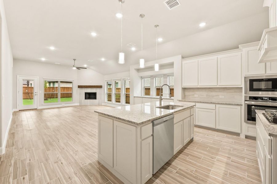 Open kitchen with white cabinets, granite island, pendant lights, and stainless appliances, open to living area with fireplace. Open kitchen with white cabinets, granite island, pendant lights, and stainless appliances, open to living area with fireplace.
