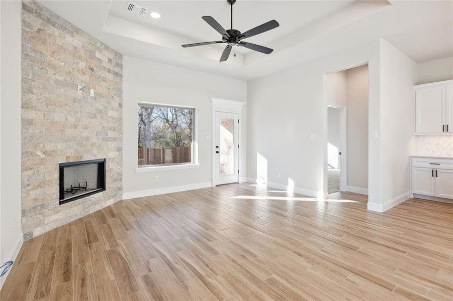 Unfurnished living room featuring a tray ceiling, ceiling fan, light hardwood / wood-style floors, and a tiled fireplace