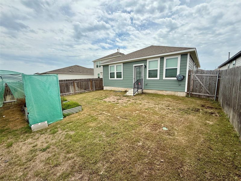 Rear exterior featuring green siding, white-trimmed windows, and a fenced yard