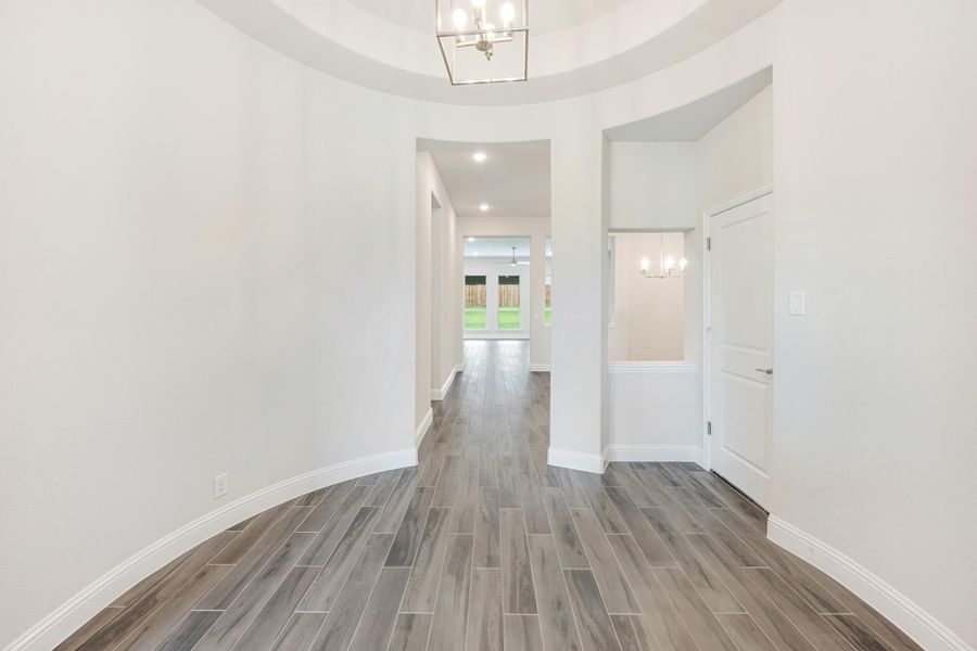 Curved entryway with tray ceiling, chandelier, and wood-look tile floors leading to main hallway