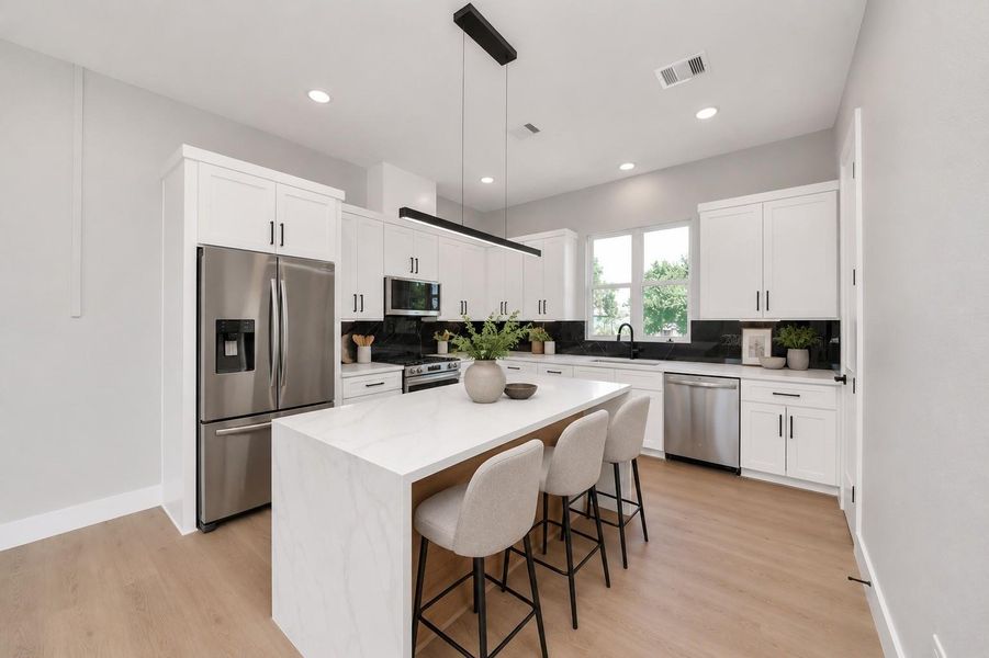 Designer kitchen featuring sleek quartz countertops, custom cabinetry, modern black accents, & a spacious waterfall island perfect for entertaining.