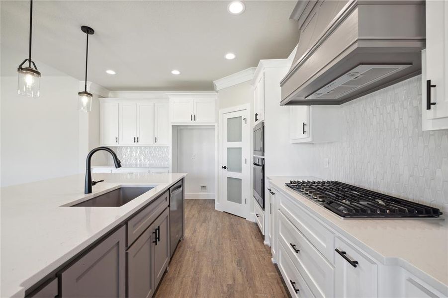 Kitchen with pendant lighting, sink, white cabinets, custom exhaust hood, and stainless steel appliances