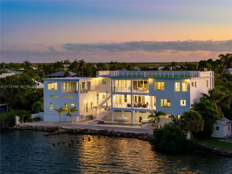 Waterfront residence featuring multi-level covered balconies, a rooftop deck with railing, a built-in pool, and a stone-lined bulkhead Waterfront residence featuring multi-level covered balconies, a rooftop deck with railing, a built-in pool, and a stone-lined bulkhead