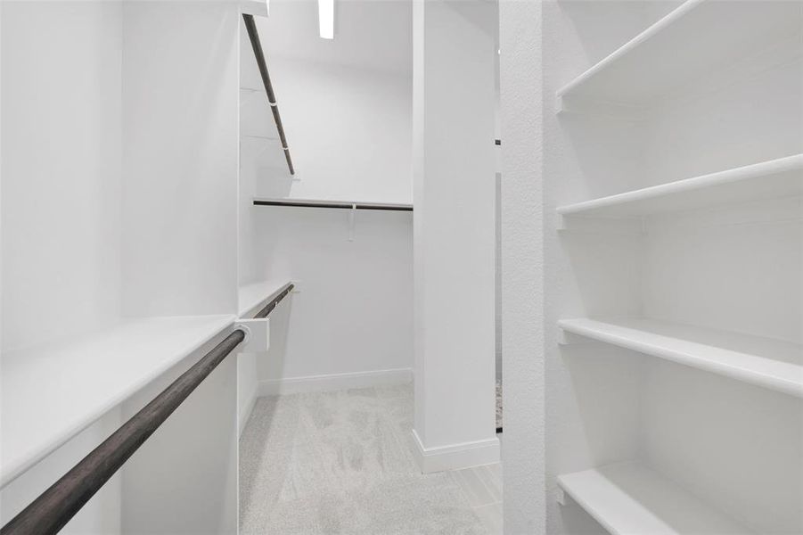 Walk-in closet featuring white built-in shelving, multiple hanging rods, and light-toned carpeting Walk-in closet featuring white built-in shelving, multiple hanging rods, and light-toned carpeting