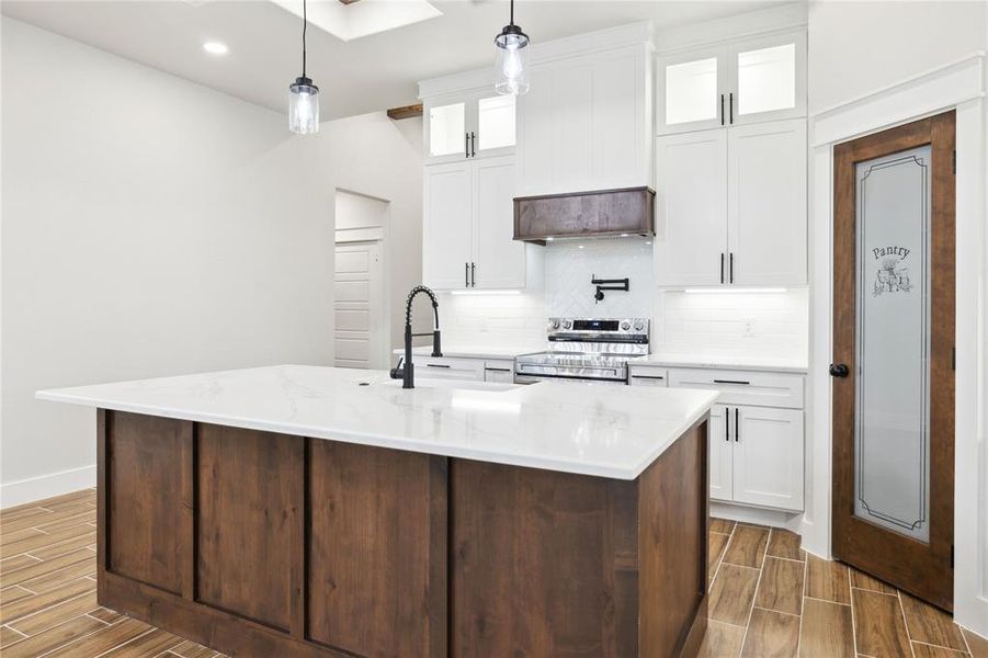 Kitchen featuring tasteful backsplash, decorative light fixtures, a center island with sink, stainless steel electric stove, and white cabinets