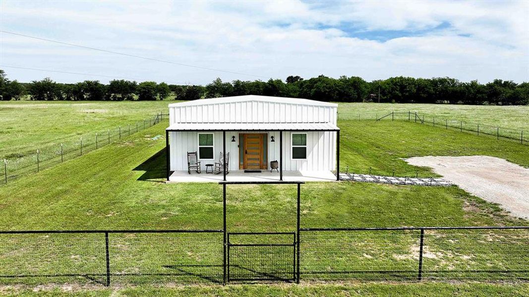 White metal-sided structure featuring a covered front porch with a wood-finish entry door