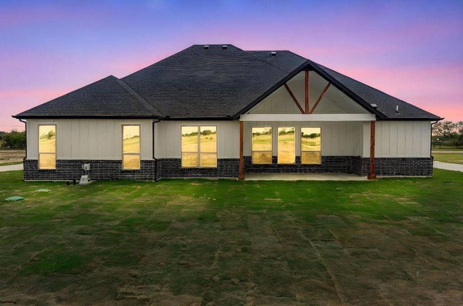 Back of house at dusk featuring a patio area, a yard, a shingled roof, and brick siding