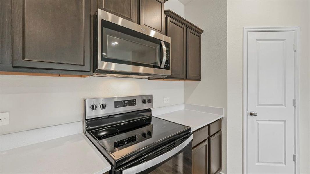 Kitchen featuring dark wood cabinetry, white countertops, stainless steel electric range, and a built-in stainless steel microwave