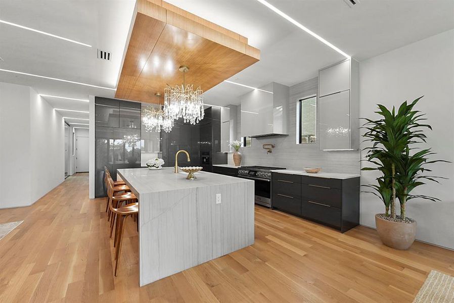 Gourmet kitchen featuring a waterfall island with integrated seating, dual crystal chandeliers, and a wood-finish ceiling accent