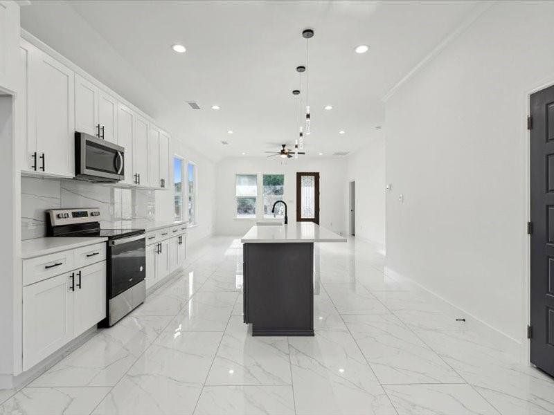 Kitchen featuring a center island with sink, light tile patterned floors, backsplash, appliances with stainless steel finishes, and white cabinets