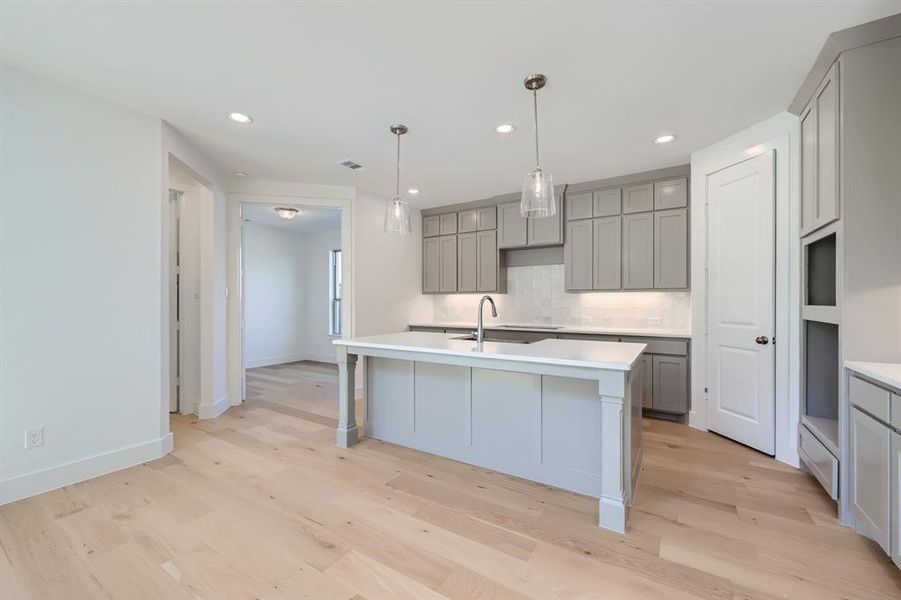 Kitchen featuring tasteful backsplash, a center island with sink, sink, decorative light fixtures, and light wood-type flooring