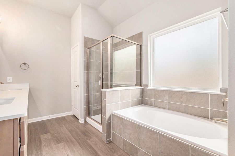 This bathroom features a modern design with a spacious walk-in shower, a large bathtub, and sleek tile flooring. The frosted window allows natural light while maintaining privacy, and the dual-sink vanity offers ample space.