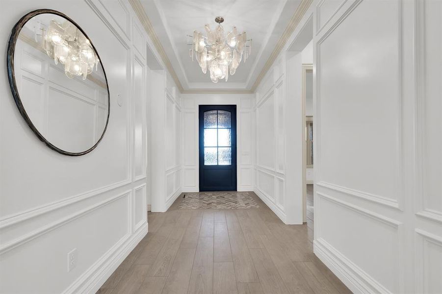 Foyer entrance with a chandelier, a decorative wall, light wood finished floors, and crown molding